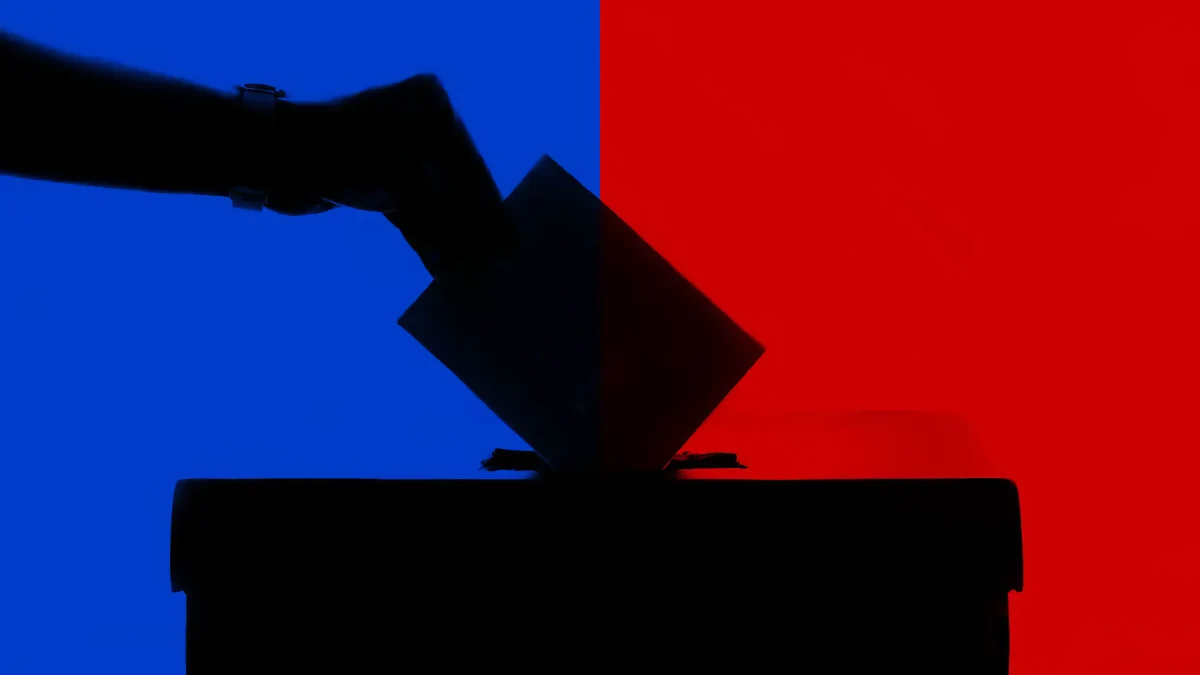 A hand dropping a ballot into a box, with a red and blue split background